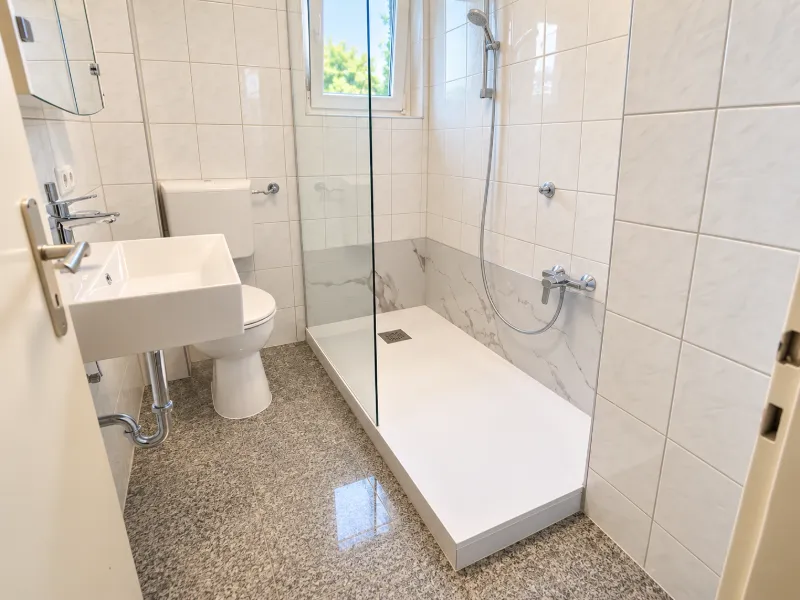 Barrierearmer Badumbau Ansbach | SeniorenBad Franken Helles kleines Badezimmer mit großer bodennaher Dusche und Glasabtrennung im Raum Ansbach.
